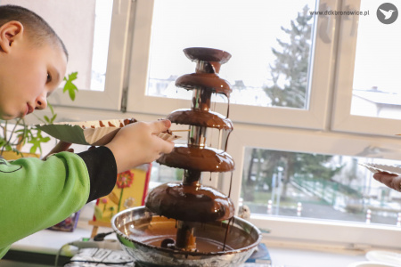 Kolorowe zdjęcie. Chłopiec nabiera laną czekoladę z maszyny do czekolady.