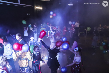 Kolorowe zdjęcie. Grupa dzieci w przebraniach tańczy z balonami na zaciemnionej sali.