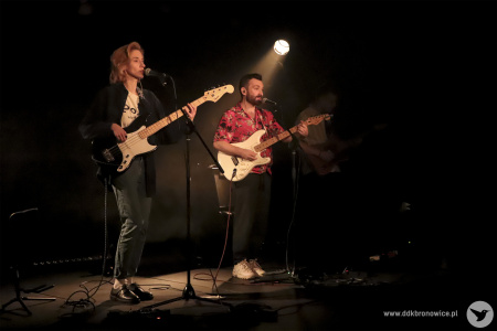 Kolorowe zdjęcie. Na scenie Aga Ozon i Adrian Kieroński - duet tworzący zespół NIEBØ. Aga gra na basie, Adrian gra na gitarze elektrycznej. Oboje śpiewają do mikrofonów na statywach.