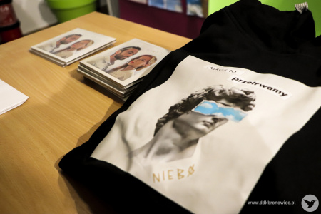 Kolorowe zdjęcie. Na stole gadżety zespołu NIEBØ. Czarna torba z beżowym kolażem z napisem: jakoś to przetrwamy i płyty.