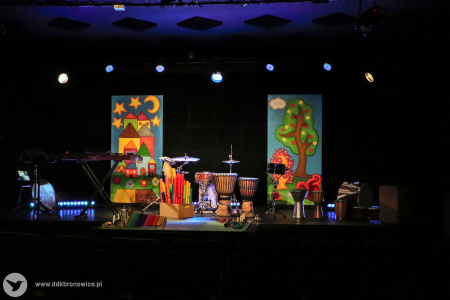Kolorowe zdjęcie. Kadr na scenę z instrumentami muzycznymi. W tle malowane kolorowe dekoracje sceniczne.