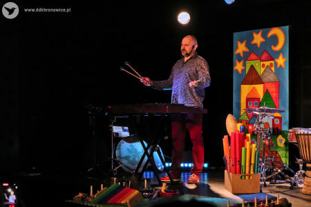 Kolorowe zdjęcie. Na scenie Marek Fedor wśród wielu instrumentów muzycznych. Muzyk trzyma w ręku pałeczki do perkusji.