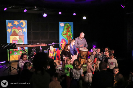 Kolorowe zdjęcie. Na scenie Marek Fedor gra na djembe. Wokół muzyka grupka dzieci.