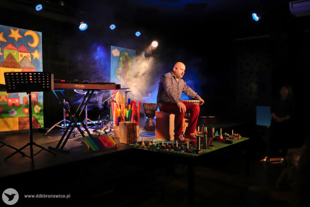 Melodia i Rytm -Kolorowe zdjęcie. Na scenie Marek Fedor wśród wielu instrumentów. Za nim kolorowe dekoracje i dym sceniczny.