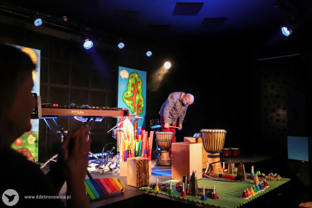 Kolorowe zdjęcie. Na scenie Marek Fedor kłania się w kierunku publiczności. Muzyk stoi pośród wielu instrumentów.