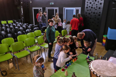 Kolorowe zdjęcie. Przed sceną dzieci grające na instrumentach. W tle puste krzesła sali kameralnej w Pracowniach Kultury Maki.