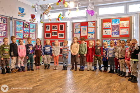 Kolorowe zdjęcie. Grupa dzieci stoi w rzędzie na tle wystawy.