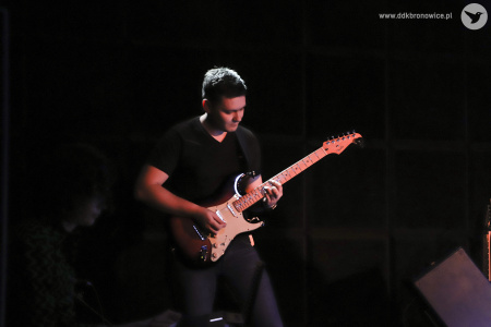 Kolorowe zdjęcie. Na scenie mężczyzna gra na gitarze.