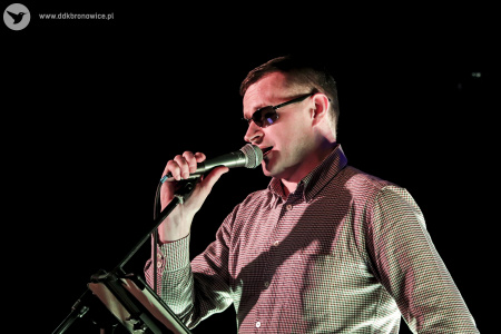 Kolorowe zdjęcie. Mężczyzna w okularach śpiewa do mikrofonu. Kadr z boku.