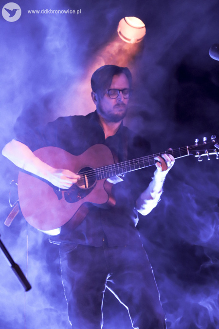 Kolorowe zdjęcie. Jurek Jurkiewicz gra na gitarze na zadymionej scenie.