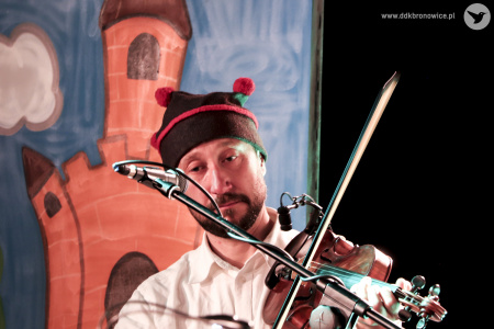 Kolorowe zdjęcie. Mężczyzna stoi i gra na skrzypcach. Na głowie ma czarną czapkę tradycyjną z trzema czerwonymi pomponami.