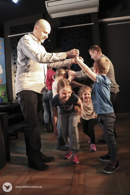 Kolorowe zdjęcie. Grupa dzieci i dwóch mężczyzn tańczą z dziećmi przed sceną.