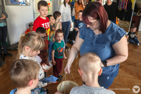 Kolorowe zdjęcie. Animatorka rozdaje dzieciom woreczki z drewnianego, okrągłego pudełka. Dzieci stoją jedno obok drugiego i czekają na ich kolej.