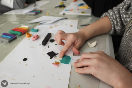 Dziewczynka tworzy swoją zabawkę. Ptak jest w kolorze białym, z pomarańczowym dziobem i czarnym cylindrem na głowie.