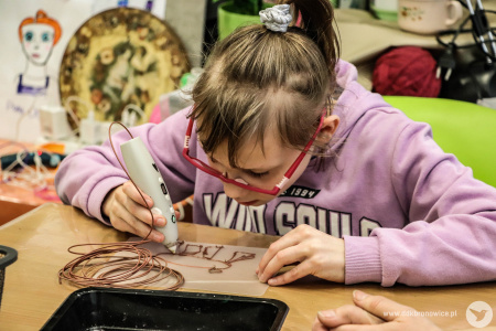 Dziewczynka tworzy swoją ozdobę używając kleju na gorąco.