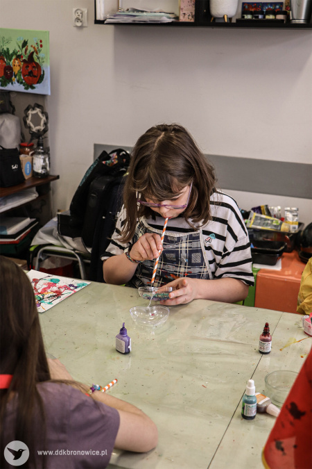 Dziewczynka maluje obraz. W tym celu wykorzystuje rurkę w buzi.