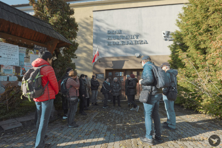 Przed wejściem do Domu Kultury Kolejarza. Grupa ludzi obrana w ciepłe kurtki. Mają ze sobą plecaki.