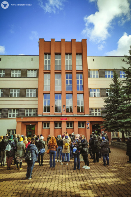 Spotkanie przed szkołą podstawową. Słonecznie. Widać niebo. Przed wejściem duża grupa uczestników.