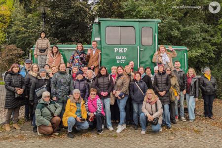 Grupowe zdjęcie uczestników spaceru z przewodnikiem. Uczestnicy uśmiechają się i machają do aparatu.