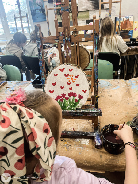 Sala warsztatowa w Dzielnicowym Domu Kultury Bronowice. Na stołach rozłożone małe sztalugi. Na sztalugach leżą okrągłe drewniane kawałki, które są malowane przez dzieci.