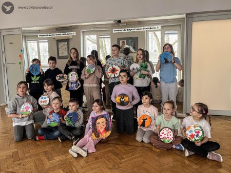 Dzieci pozują z ukończonymi obrazami na drewnie. Dzieci uśmiechają się. Obrazy przedstawiają kolorowe krajobrazy. Jeden obraz przedstawia twarz.