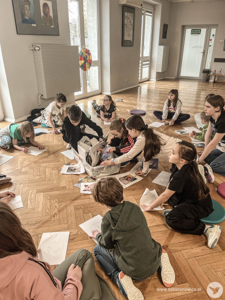 Dzieci siedzą na podłodze i uczestniczą w kolejnej zabawie animacyjnej. Mają przed sobą białe kartki, na których muszą stworzyć rysunek.