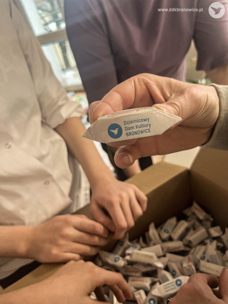 Pudełko z krówkami. Cukierki są białe i mają niebieskie logo DDK Bronowice - biały koliber na niebieskim tle.