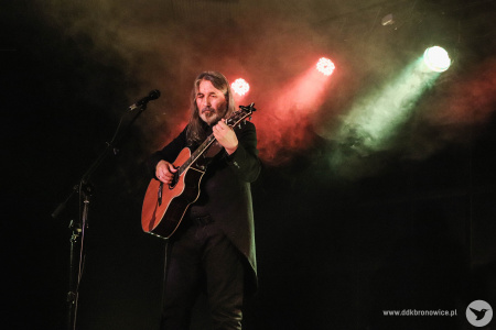 Jan Kondrak gra na scenie na gitarze. Światła na scenie czerwono-zielone.