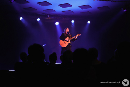 Na scenie niebieskie światło. Muzyk oświetlony jest jednym punktowym światłem. Artysta wykonuje piosenkę na środku sceny.