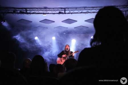 Na pierwszym planie widać kontury publiczności. W tle na scenie Jan Kondrak wykonuje piosenkę. Na scenie niebieskie światło.