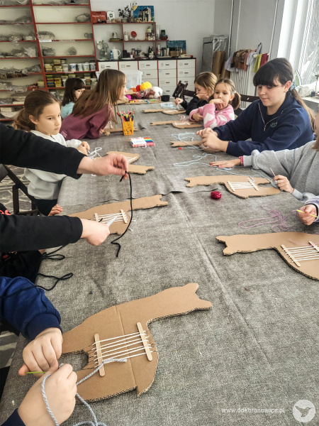 Przy stole siedzą dzieci. Tworzą ozdoby w kształcie lamy. Kontury zwierzęcia wycięte są z tektury.