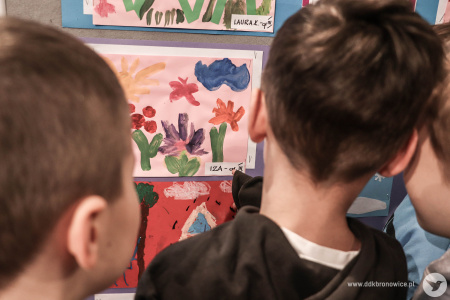 Chłopcy oglądają obraz. Obraz przedstawia kolorowe kwiaty, żółte słońce i niebieską chmurę.
