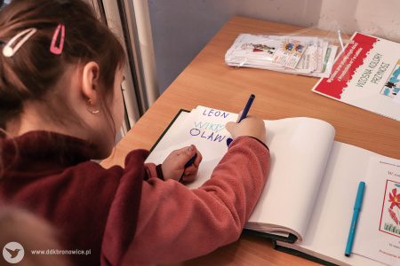 Dziewczynka w czerwonej bluzie wpisuje się do księgi gości.