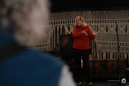 Po lewej stronie kontury osoby na widowni. Po prawej, aktorka mówiąca na scenie.