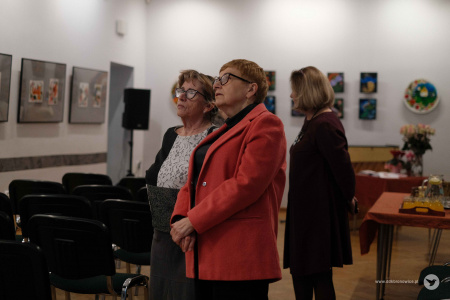 Dwie starsze kobiety oglądają wystawę obrazów. Panie rozmawiają ze sobą.