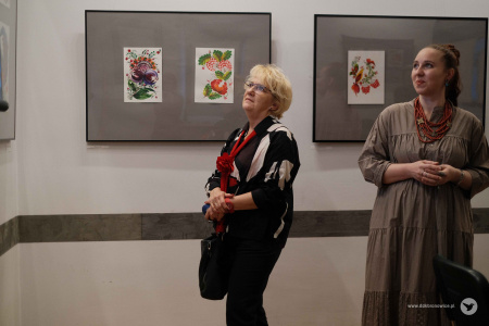 Po lewej stronie kobieta ogląda wystawę. Po prawej stronie stoi Olena Kovalenko.