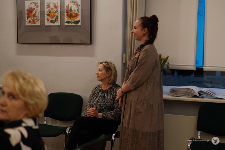 Przy ścianie siedzi Ewa Rejmak. Obok niej stoi instruktorka grupy Olena Kovalenko.