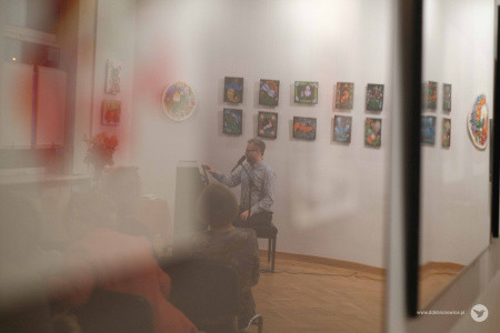 W odbiciu szyby widać pianistę i publiczność.