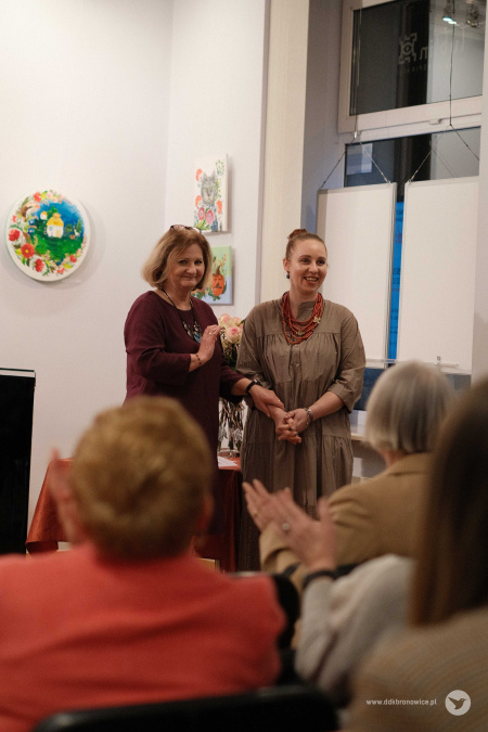 Pani dyrektor ubrana w bordową sukienkę trzyma za rękę Olenę Kovalenko. Instruktorka uśmiecha się.