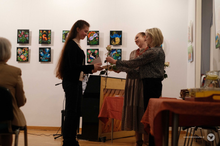 Autorka obrazów ubrana na czarno odbiera dyplom i kwiaty.