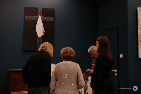 Trzy kobiety i jeden mężczyzna oglądają obraz przedstawiający krzyż i białą chustę.