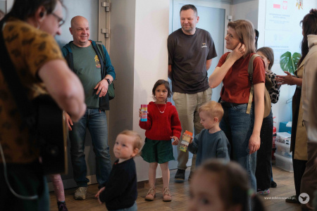 Na pierwszym planie gitarzysta. W tle uczestnicy słuchają muzyki. Mały chłopczyk patrzy na gitarzystę.