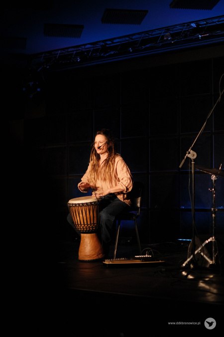Sala teatralna. Pojedyncze światło oświetla Sylwię Lasok. Ubrana jest w beżową koszulę. Między nogami trzyma bęben.