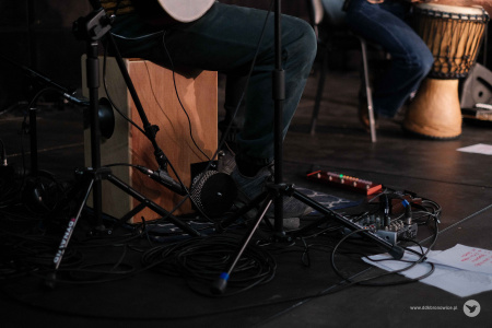 Scena. Widać tylko nogi muzyka i kable. Muzyk siedzi na cajonie. Obok niego leży mała konsola muzyczna.