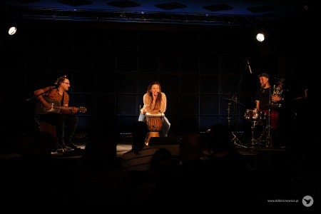 Na środku wokalistka mówi do widowni. Po lewej stronie siedzi gitarzysta. Po prawej stronie jest perkusista i trzyma w rękach euphonium. Muzycy są podświetleni żółtym, pojedynczym światłem.