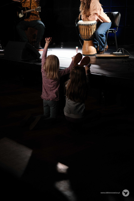 Dwie dziewczynki bawią się pod sceną. Machą do muzyków.