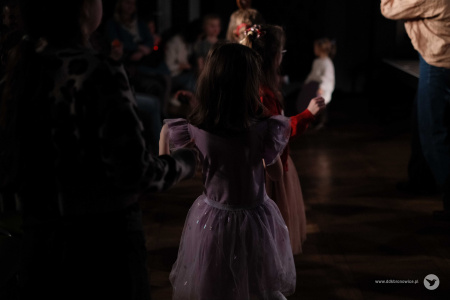 Pod sceną stoi dziewczynka w fioletowej sukience.