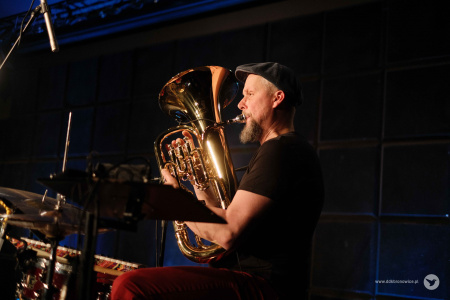 Muzyk w czarnej koszulce i czerwonych spodniach gra na euphonium.