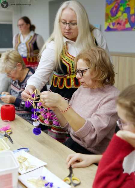 Iwona Barecka pomaga jednej z uczestniczek. Ozdoba jest koloru niebieskiego, fioletowego i różowego.