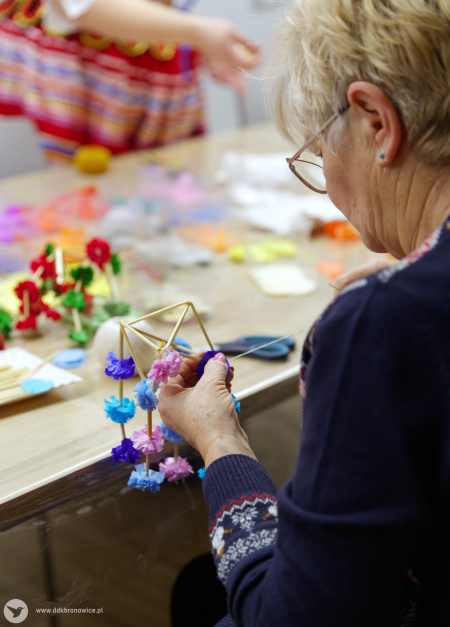 Starsza uczestniczka warsztatów w granatowym swetrze kończy tworzyć swoją niebiesko-fioletową ozdobę.